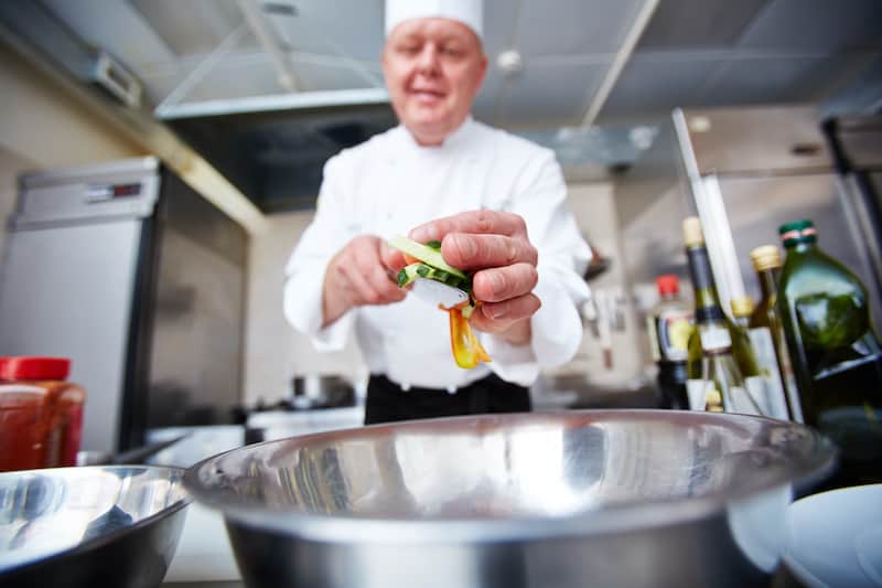 Image of male chef putting cut vegetables in bowl in the kitchen